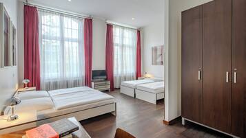 A hotel room with two beds, a TV, a desk with a lamp, and a wardrobe.