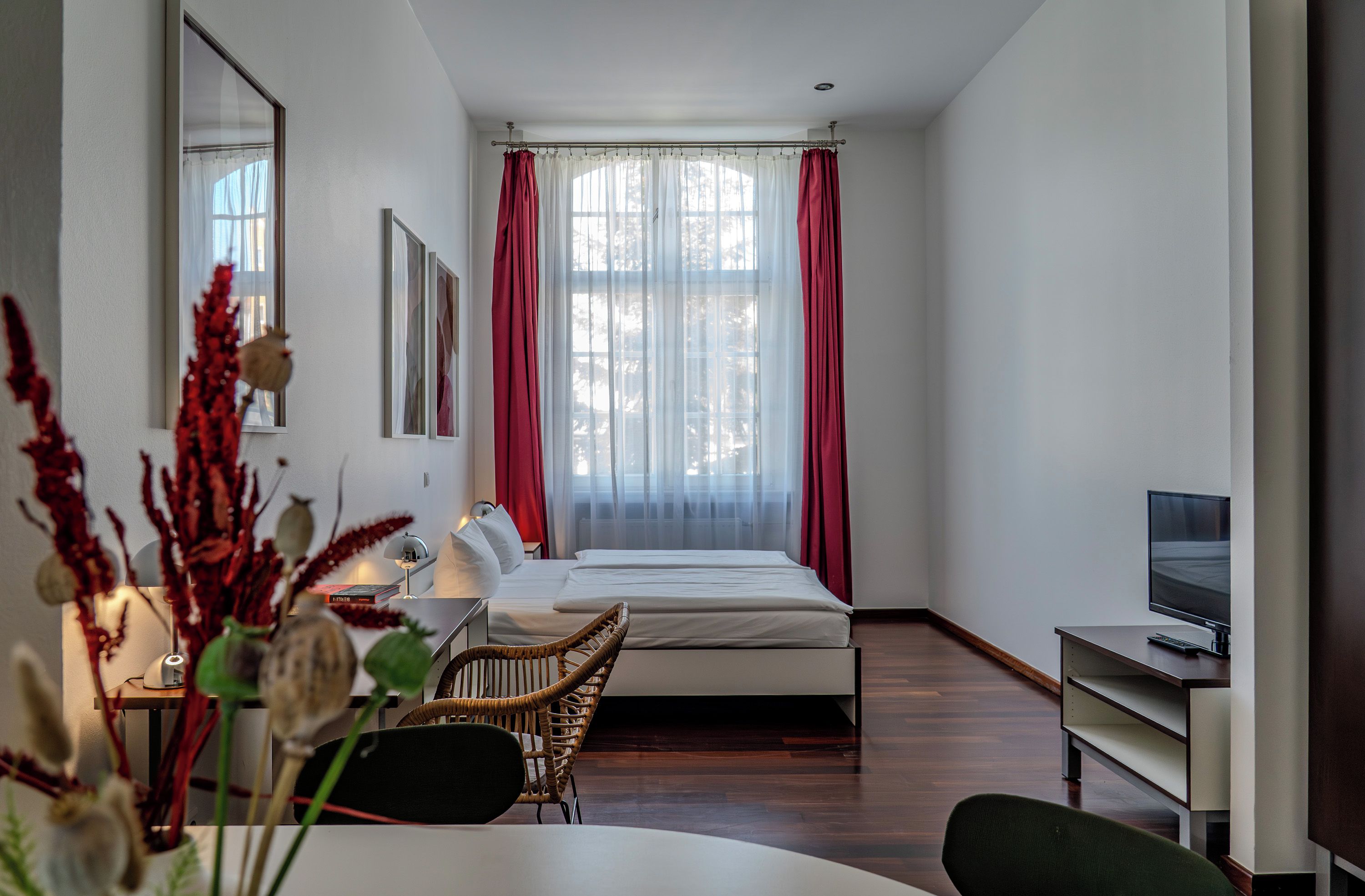 A hotel room with a bed, a desk with a chair, a television, and a window with curtains.