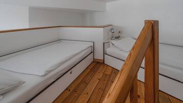 Une petite pièce compacte avec un plancher en bois, un lit superposé, une table de chevet avec une lampe et une prise de courant.