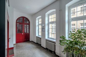 A hallway with a red door, white walls, and large windows. - GLS Campus Hotel (Berlin)