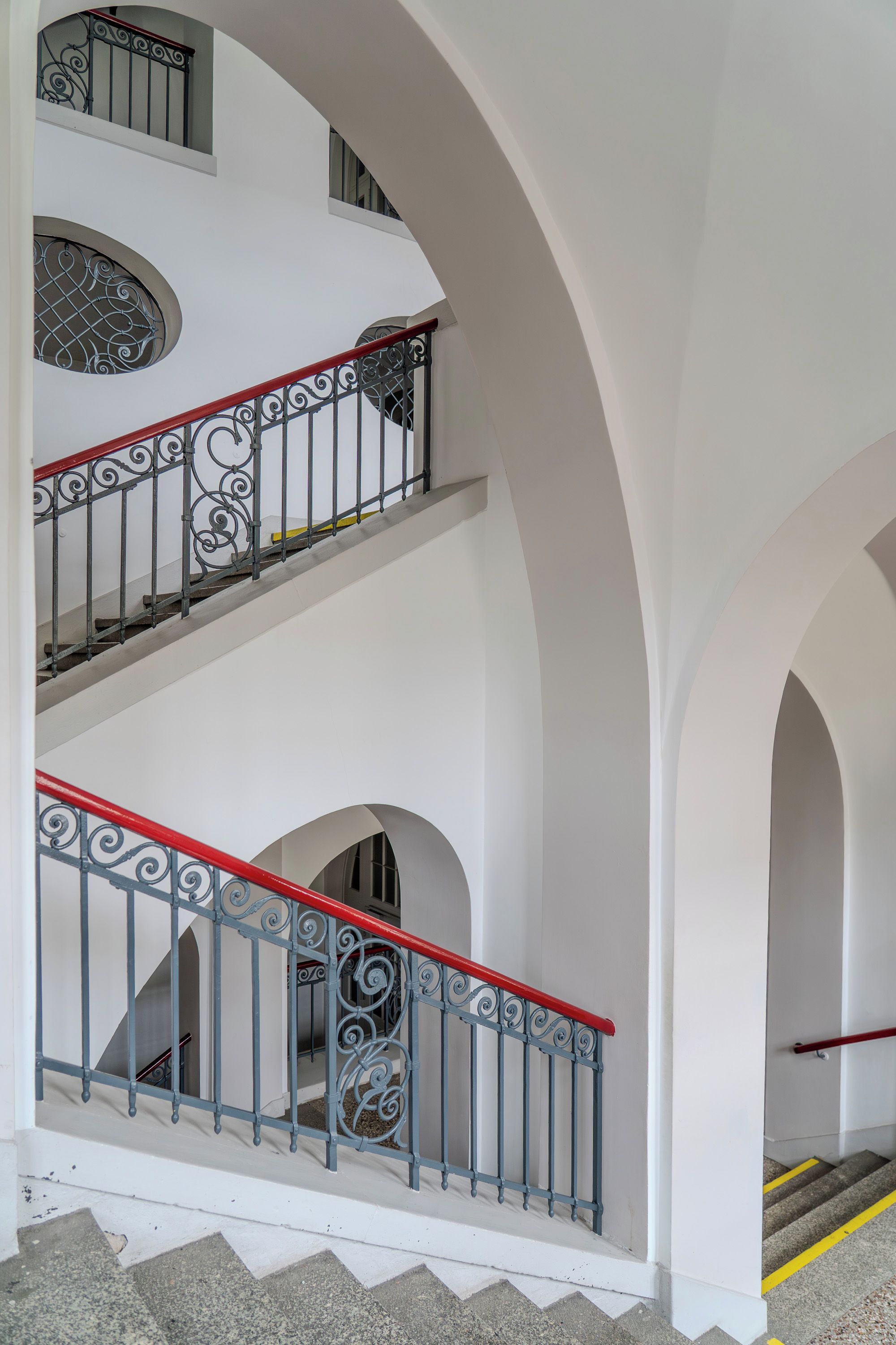 Ein mehrgeschossiges Interieur mit weißen Wänden und einer Treppe mit aufwendiger Metallgeländerung.