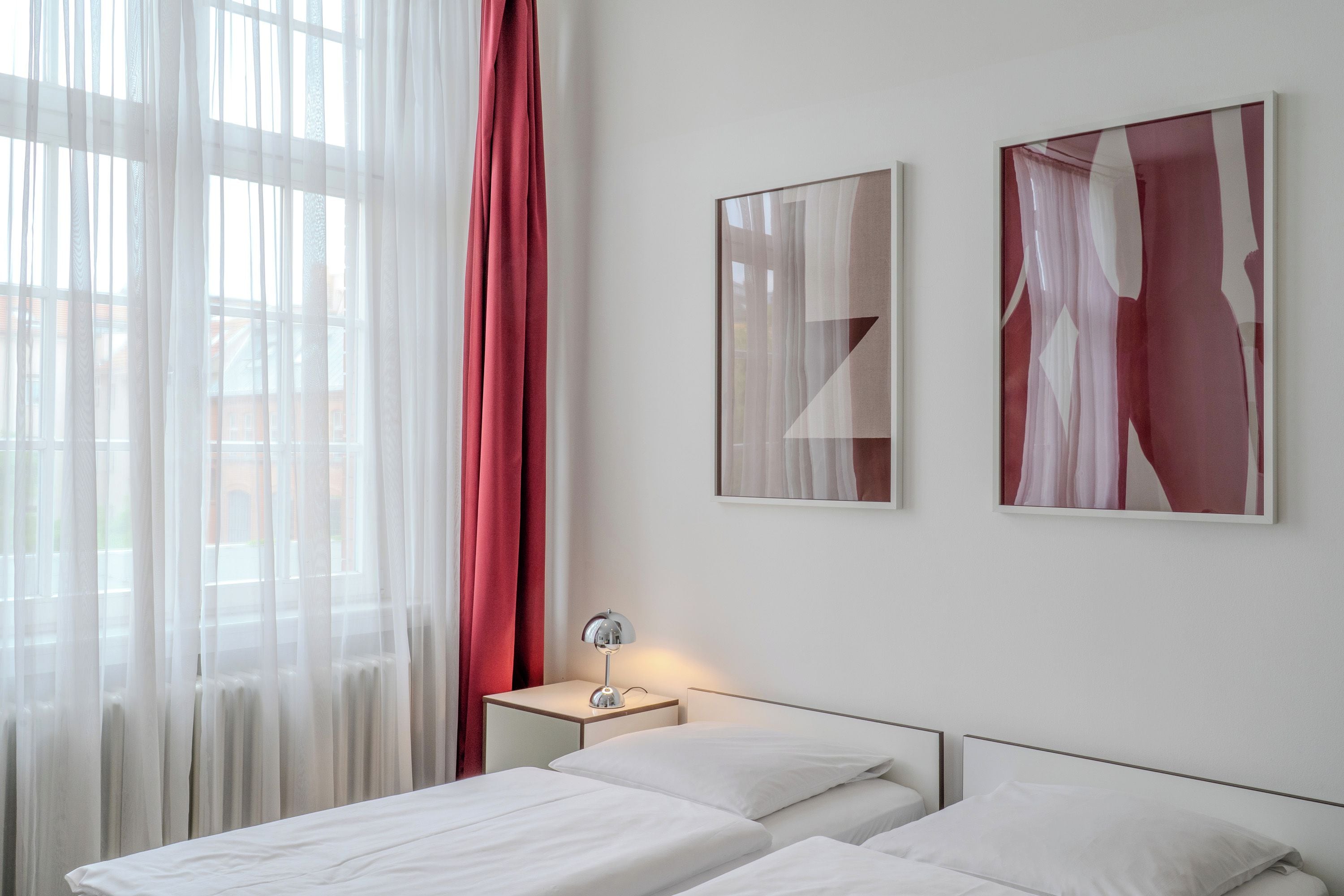 Ein Hotelzimmer mit zwei Betten, einem Nachttisch mit Lampe und zwei abstrakten Bildern an der Wand.