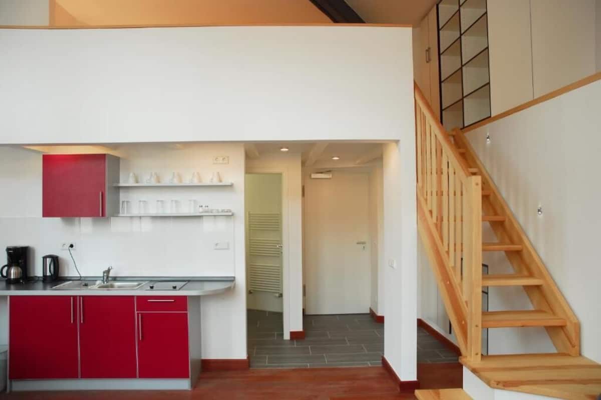 Una cocina moderna con armarios rojos, una escalera de madera y vista al área de estar.