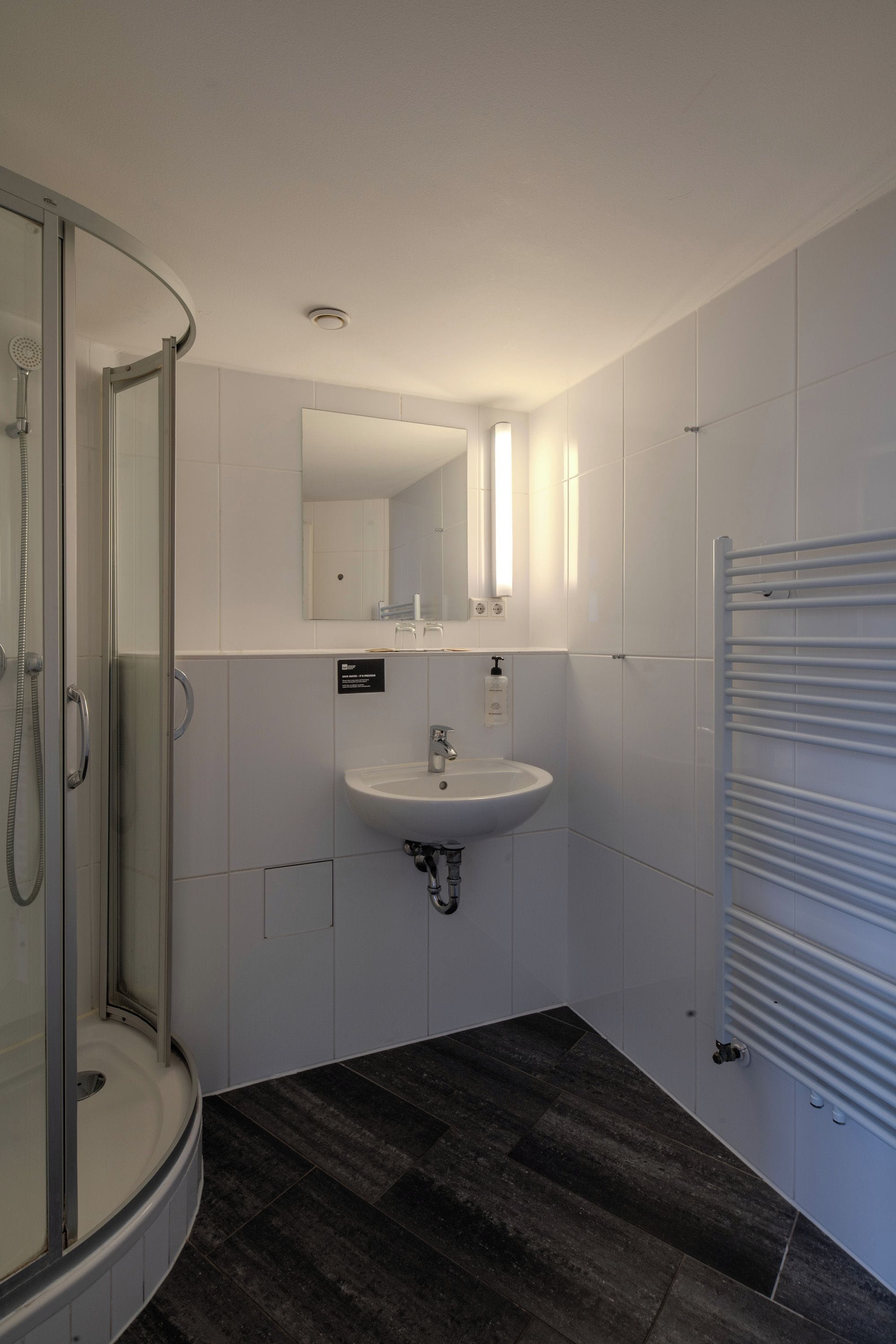 Ein modernes Badezimmer mit einer Duschkabine aus Glas, einem weißen Waschbecken und einem Spiegel darüber.