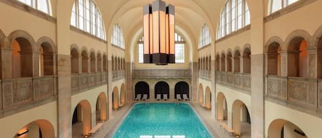 A large indoor swimming pool with arched ceilings and a central chandelier.