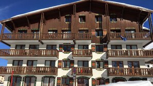 Un edificio de madera de varios pisos con balcones, una pista de esquí al frente y un letrero que indica un chalet.