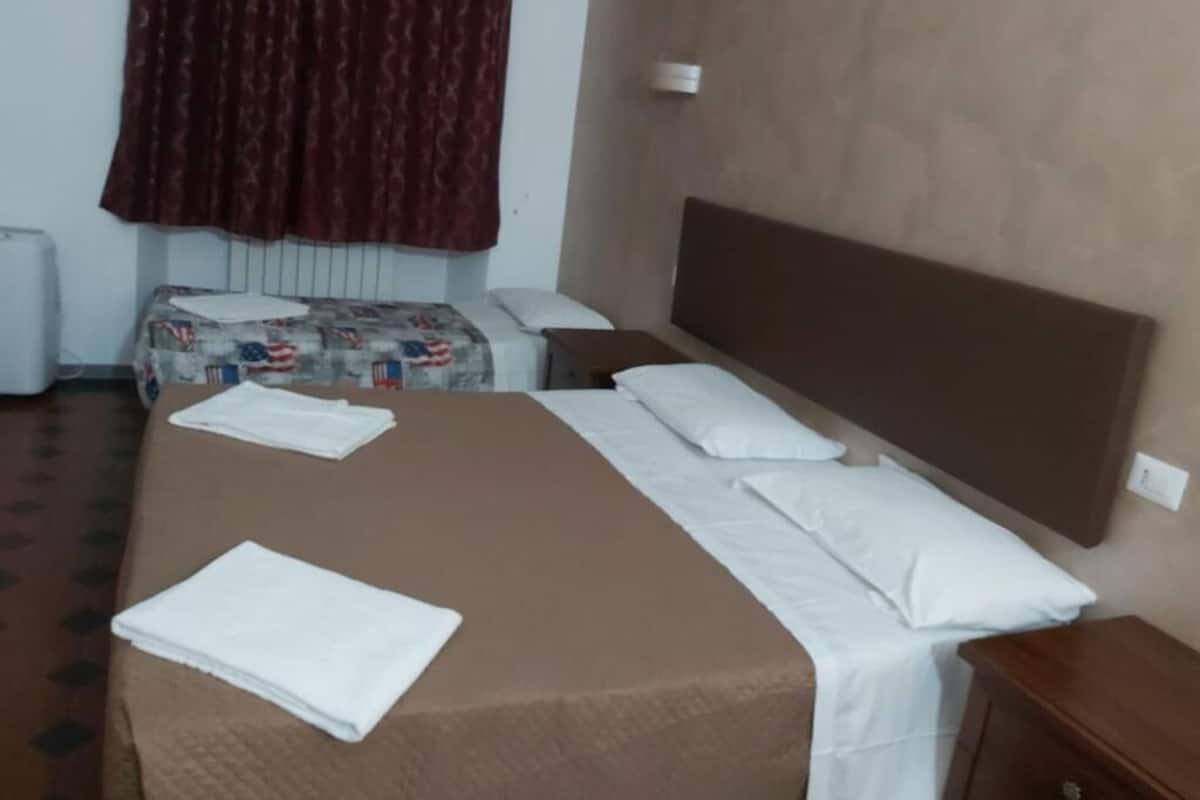 A hotel room with a bed, a nightstand, a wall socket, and a radiator.