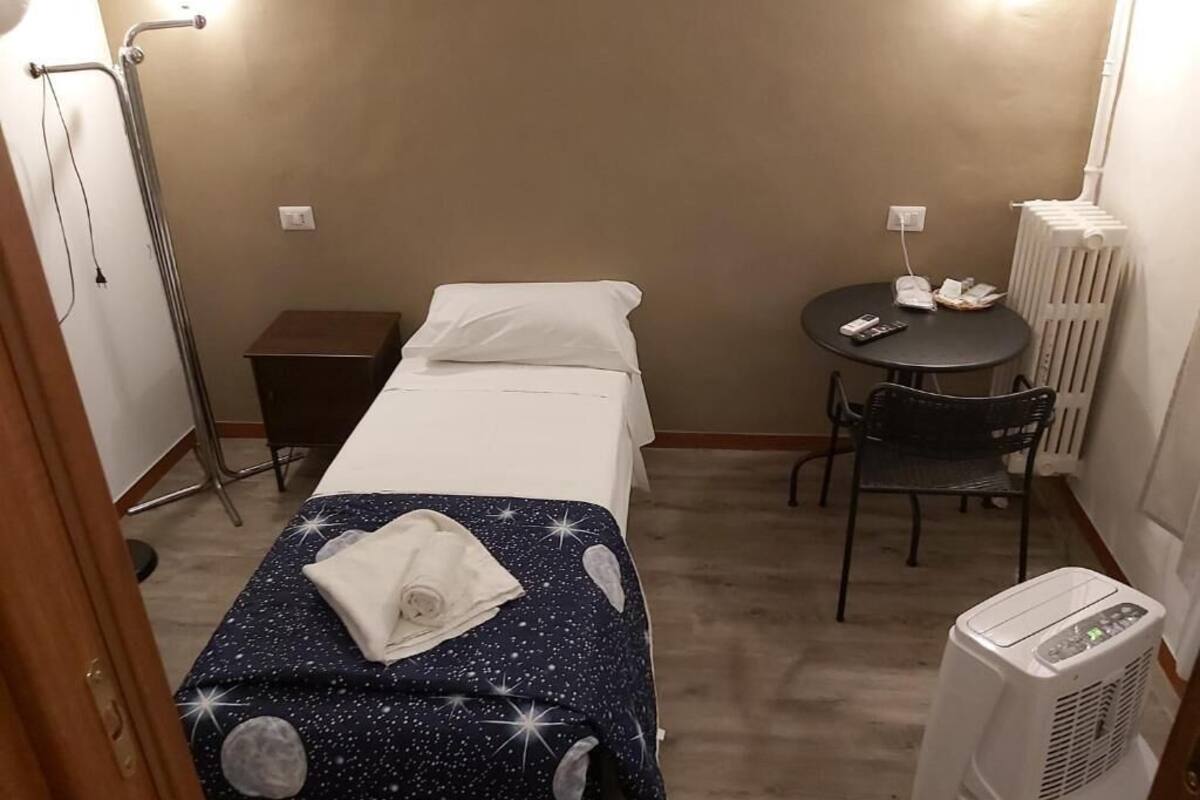 A small hotel room with a bed, a chair, a table, and a radiator.