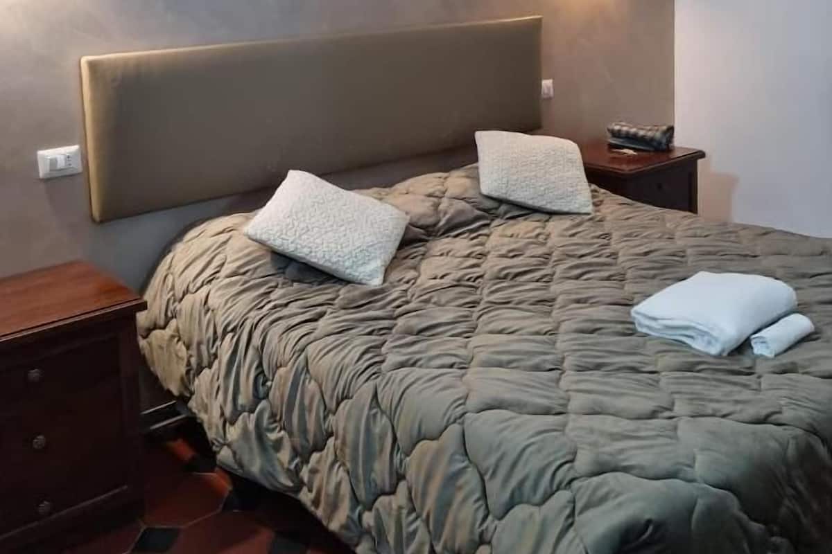A bedroom with a large bed, two bedside tables, and wall-mounted lighting.