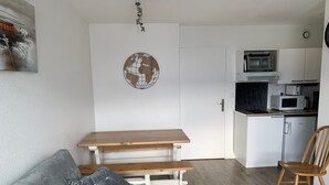 Un espace de vie compact comprenant un coin cuisine, une table à manger en bois avec des bancs, un canapé gris et un globe décoratif accroché au mur.