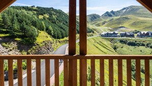 Une vue depuis un balcon en bois donnant sur un paysage montagneux, avec une route et des bâtiments.