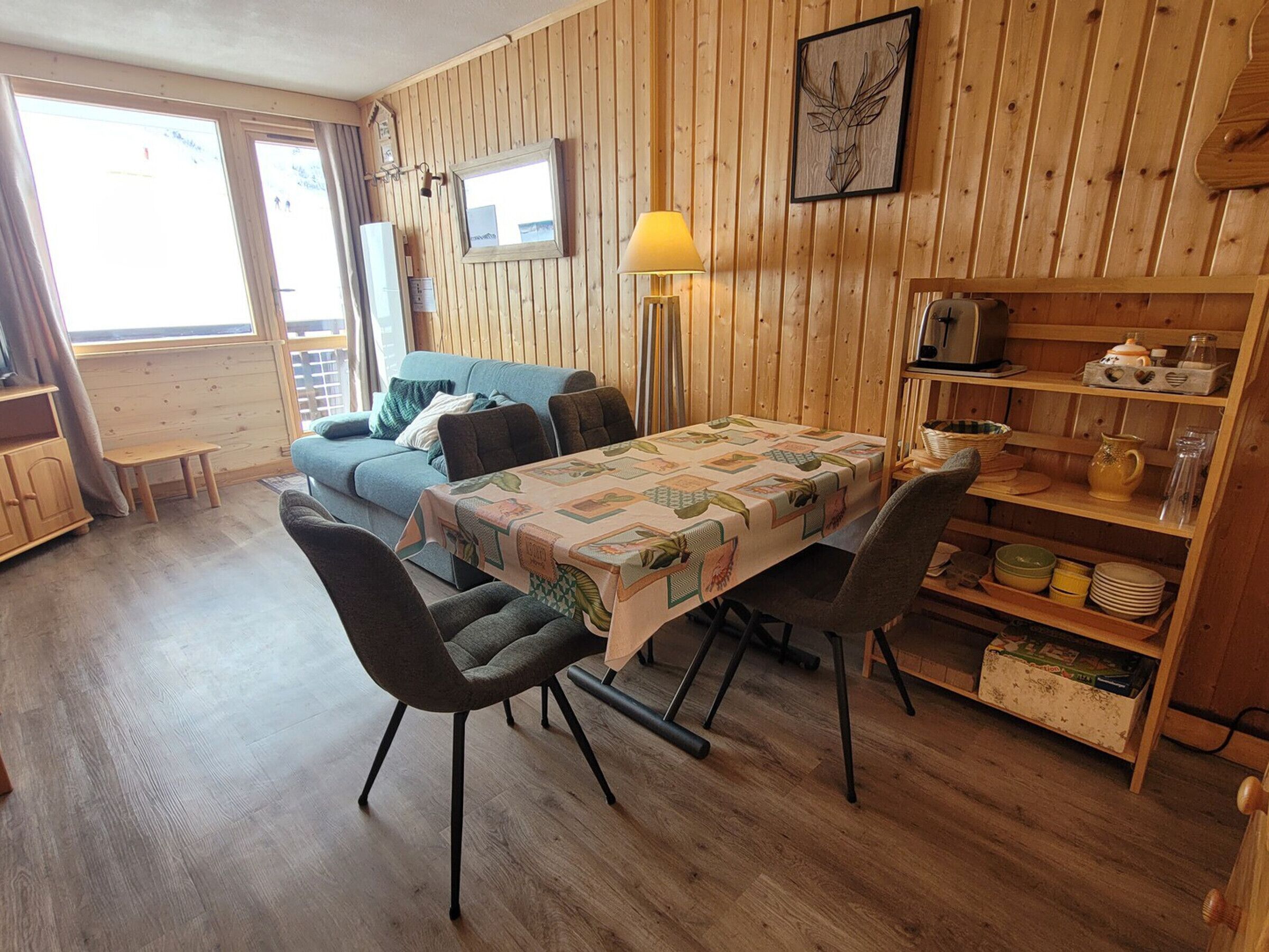 A cozy room with a wooden interior, a dining table with chairs, a sofa, and a lamp.