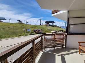 A balcony with a view of a ski lift and a small cabin on a grassy hill.