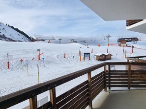A snow-covered ski slope with ski lifts, a wooden deck, and a view of the mountains.