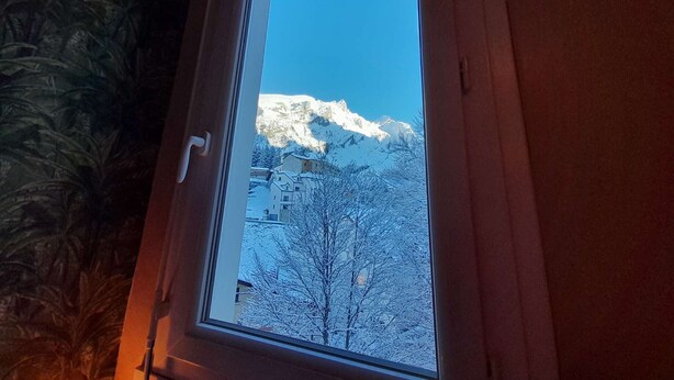 Janela com vista para montanhas cobertas de neve e árvores sem folhas.