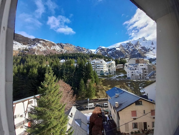 A mountain village with snow-capped peaks, dense forests, and modern buildings with balconies.