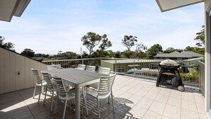 A patio with a table and chairs, a barbecue grill, and a view of trees and buildings in the background.
