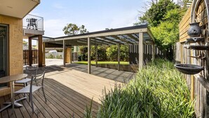 A covered outdoor patio with a wooden deck, a table and chairs, and a garden area with plants and a bird bath.