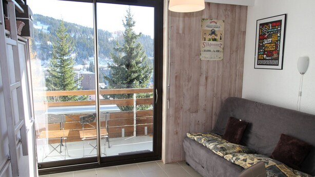 A cozy living room with a grey sofa, a wooden dining table, and a view of a snowy mountain through a sliding glass door. - Renovated well-equipped studio, south exposure, Chamrousse (Chamrousse)