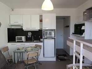 Une cuisine compacte avec des meubles blancs, un four à micro-ondes, un réfrigérateur et un coin repas comprenant une table et des chaises.