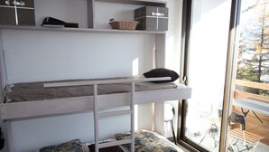 A bunk bed with storage shelves above, a window with a view of outdoor furniture, and a door to the right. - Renovated well-equipped studio, south exposure, Chamrousse (Chamrousse)
