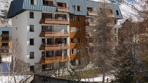 A multi-story building with balconies, set against a mountainous backdrop.