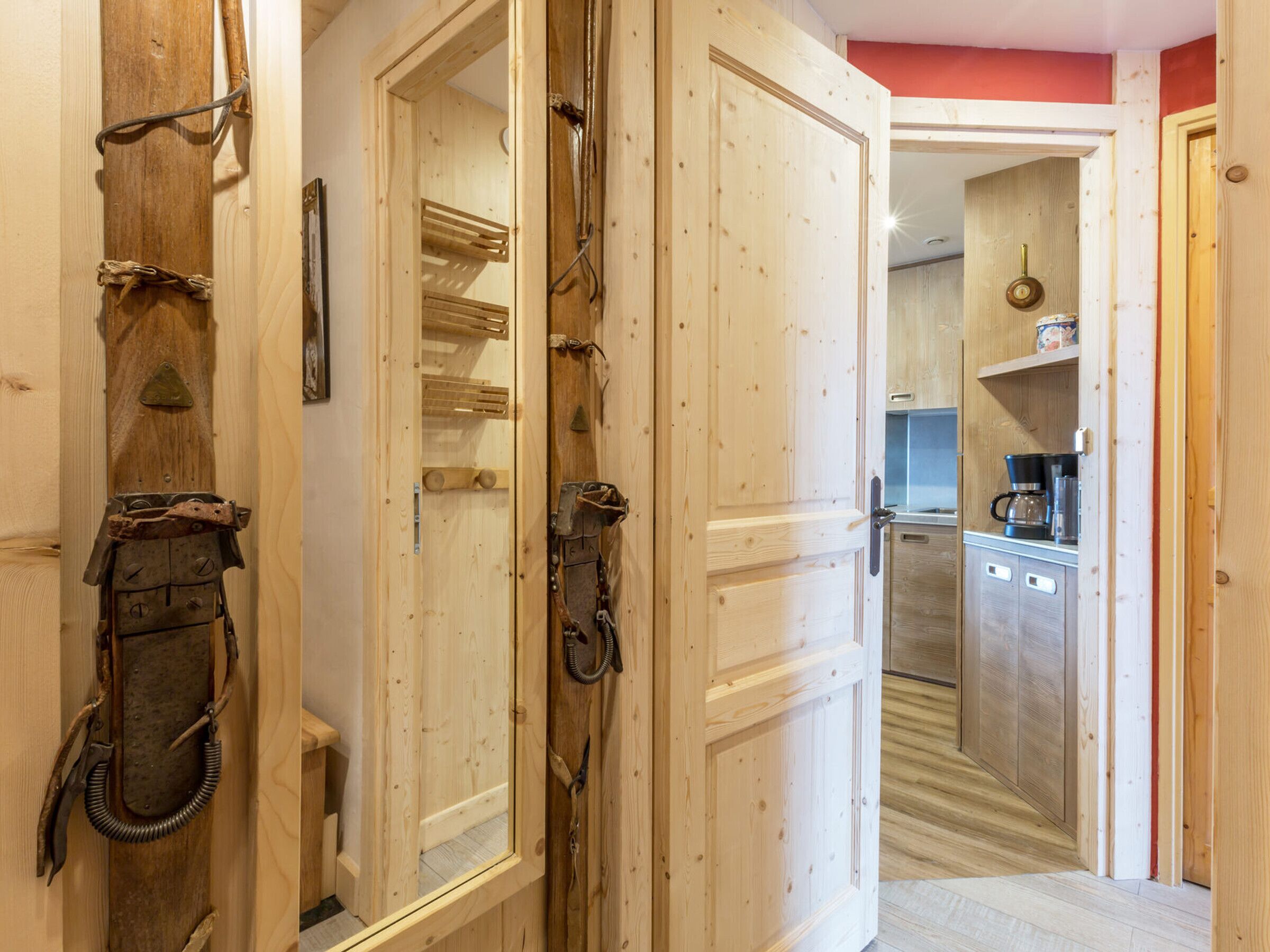 A wooden interior with a kitchen area visible through an open door.