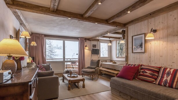 A cozy living room with wooden beams, a sofa, a coffee table, and a dining area.