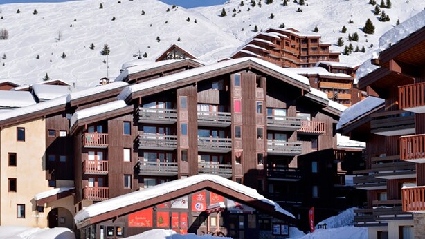 Un hotel de varios pisos con balcones de madera y techos cubiertos de nieve, con una montaña nevada como fondo.