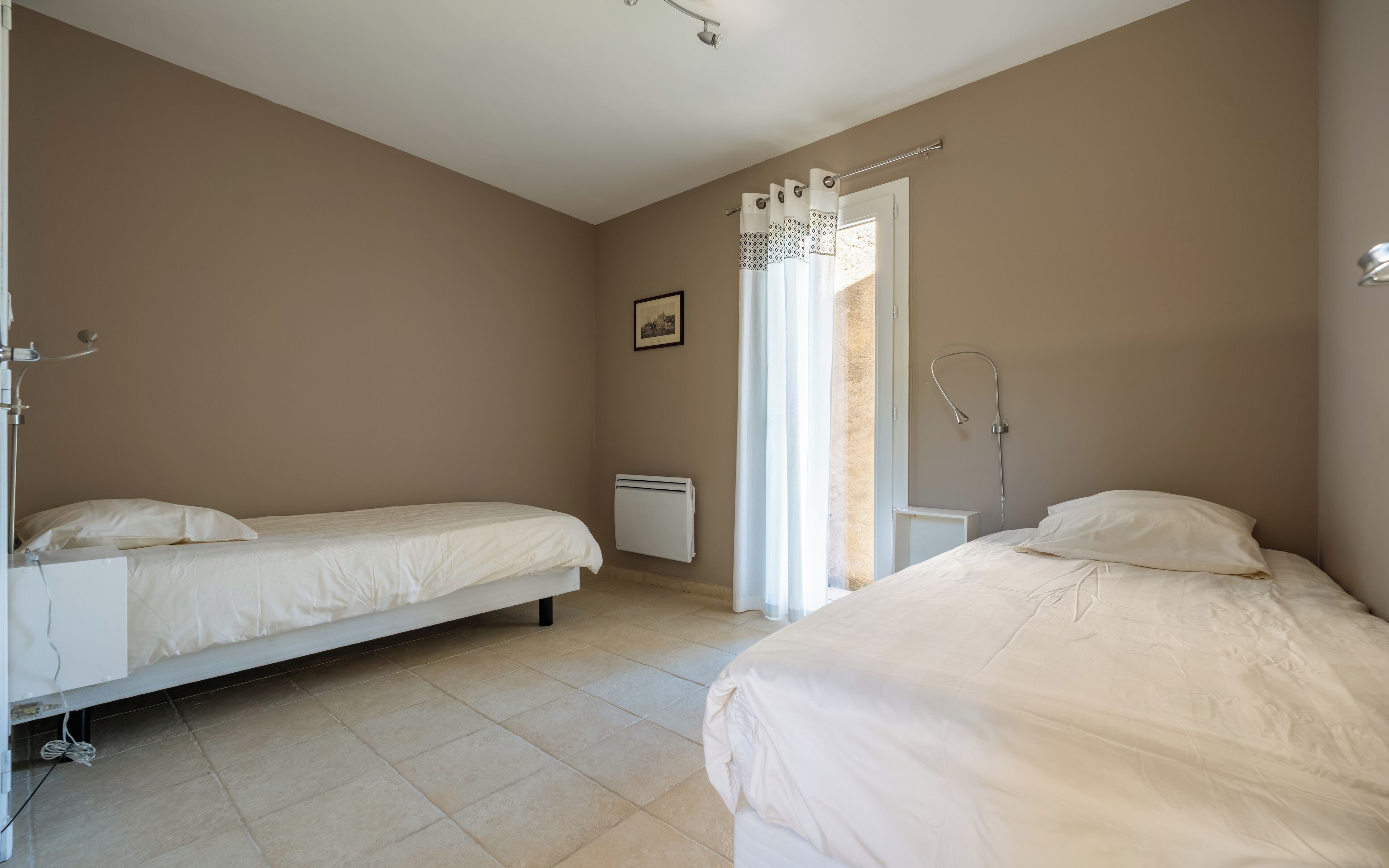 Quarto com duas camas, um radiador, um chuveiro e uma janela com cortinas.