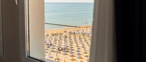Vista de una playa a través de una ventana, mostrando una playa arenosa con numerosos sombrillas y sillas de playa.