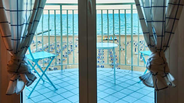 Ein Balkon mit Blick auf den Strand, ausgestattet mit blau-weißen Streifenmarkisen und Tischen.