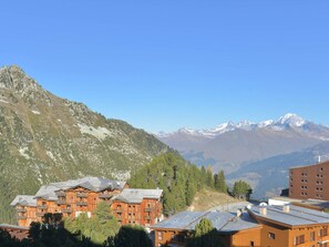 Eine Berghütte mit mehreren Holzhäusern, umgeben von üppigem Grün und schneebedeckten Bergen im Hintergrund.