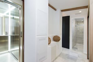 A hallway with a glass elevator, a white door, and a shower area with a glass door.