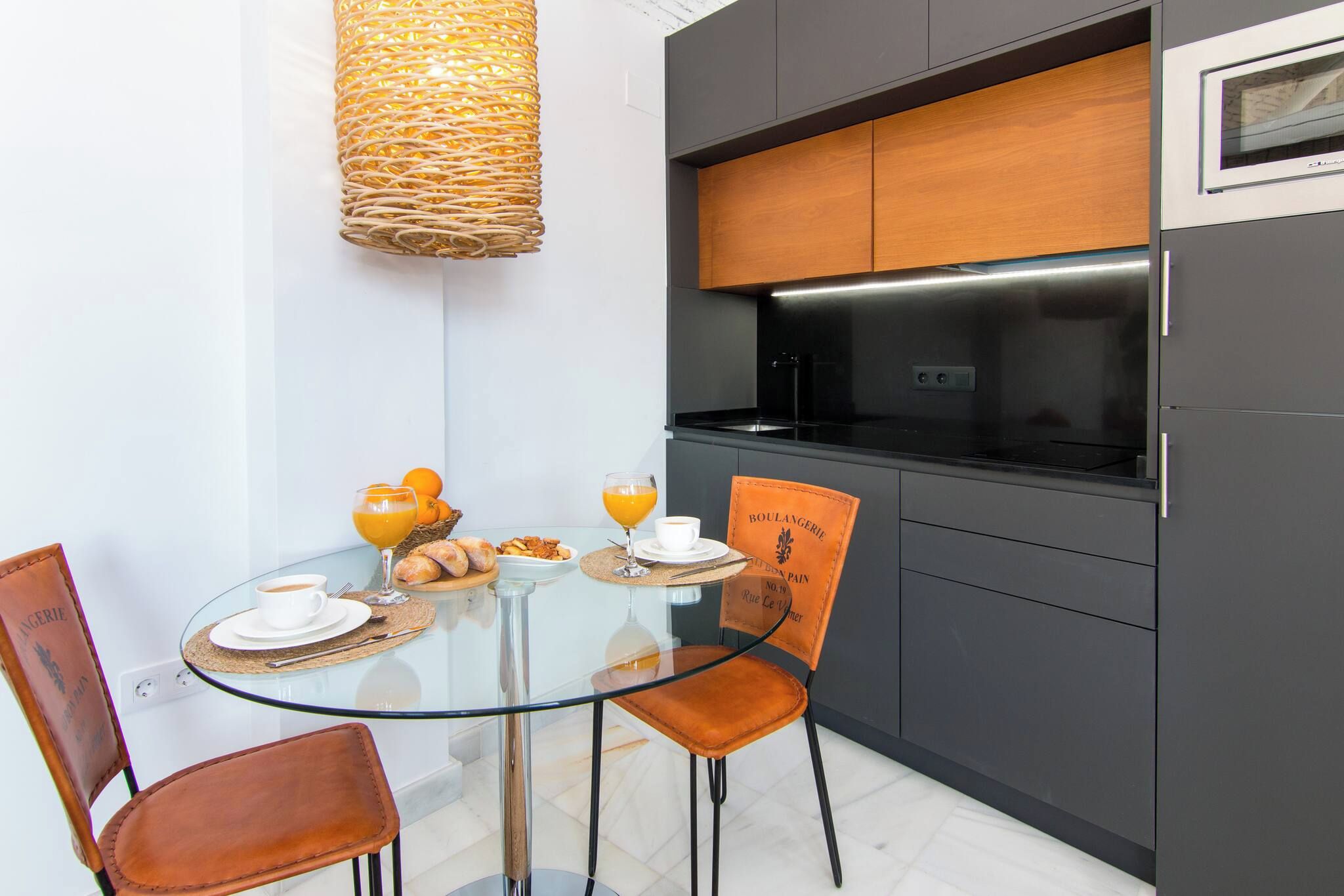 A modern kitchen with a glass dining table, two chairs, and a hanging light fixture.