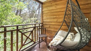 Une cabane en bois avec une chaise suspendue et une petite table, donnant sur une zone boisée.