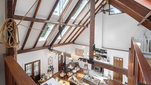 Un loft spacieux avec de hauts plafonds, des poutres apparentes, des fenêtres de toit, un coin repas, une cuisine et une cheminée.