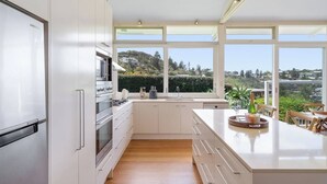 A modern kitchen with white cabinetry, stainless steel appliances, and a large island with a view of a hillside. - 'The Bungan' - Absolute Beachfront, Direct Beach Access to Bungan Beach, Newport (Newport)