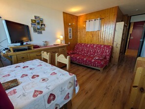 Quarto aconchegante com parede de madeira, televisão, sofá e mesa de jantar.