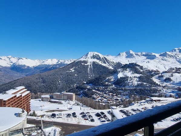 A snow-covered mountain landscape with a town in the foreground, featuring buildings and a parking area.