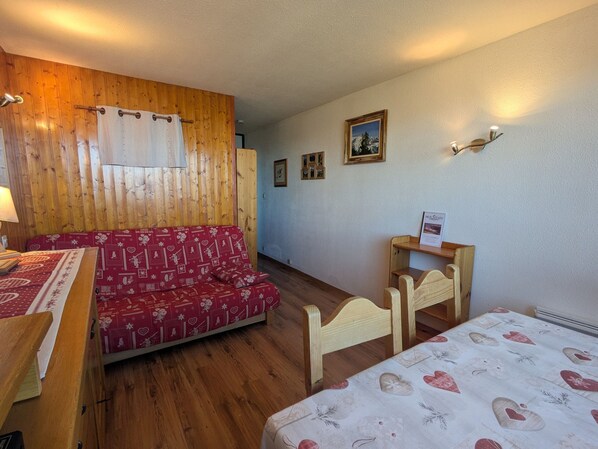 Una habitación con pared de madera, un sofá rojo estampado, una cama de madera y una mesita con un cartel.