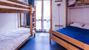 Une chambre de dortoir avec des lits superposés, une porte donnant sur un espace extérieur et une étagère avec des serviettes pliées.