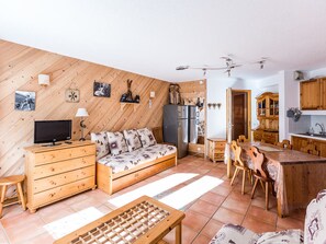 A cozy, well-lit living room with a sofa, TV, wooden furniture, and a kitchen area with wooden cabinets and a dining table. - Cozy 2-Room Apt in Montchavin, Close to Slopes, Balconies, Free Parking, Sleeps 5 (La Plagne Montchavin Les Coches)