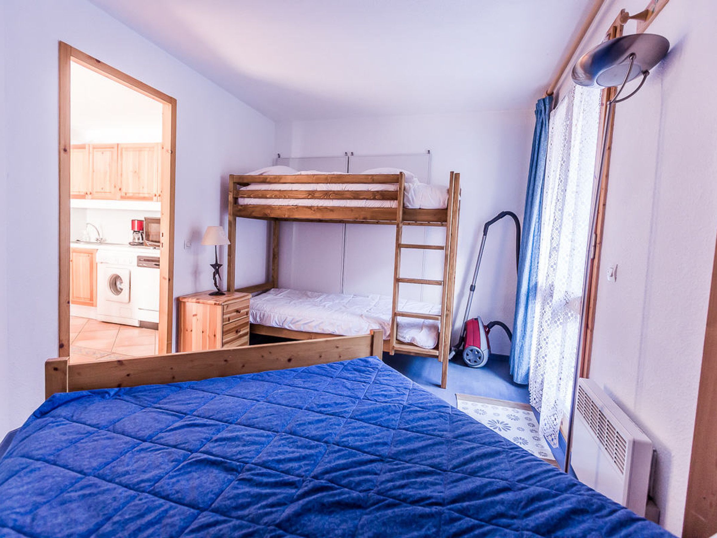 Une petite pièce comprenant un lit superposé, un bureau, une chaise, une lampe et un aspirateur.