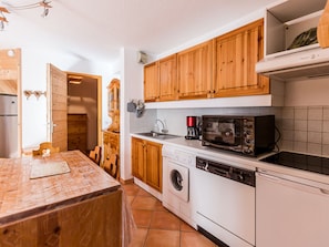 A compact kitchen with wooden cabinets, a microwave, a coffee maker, and a washing machine.