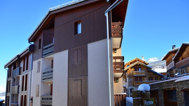 Un immeuble à plusieurs étages, avec une base en pierre et des étages supérieurs en bois, doté de balcons et d’une enseigne indiquant qu’il s’agit d’une pharmacie.