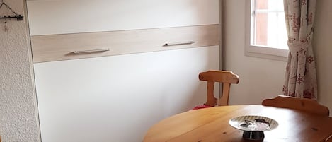 Una habitación con una mesa de comedor de madera, un armario blanco y una ventana con cortinas.