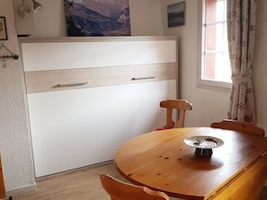 Ein Zimmer mit einem Holzespeisetisch, einem weißen Kleiderschrank und einem Vorhangfenster.