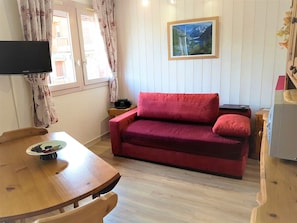 Ein gemütliches Zimmer mit einem Holzesstisch, einem roten Sofa, einem Flachbildfernseher und einem Gemälde einer Berglandschaft.