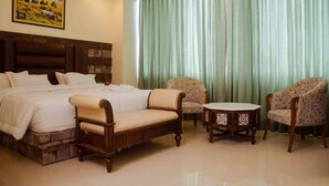 A hotel room with a large bed, two armchairs, a small round table, and a green curtain. - Grand Lotus Dimapur (Dimapur)
